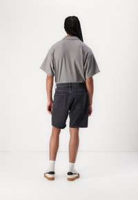 Grå kortärmad skjorta med ett strukturerat mönster, parat med mörka denimshorts och avslappnade sneakers, sedd bakifrån.