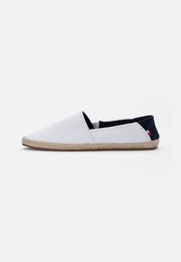 Hvit lerrets espadrille med spiss tå, elastiske sidestykker og såle av naturlig jute-seil. Har en marineblå aksent ved hælen.