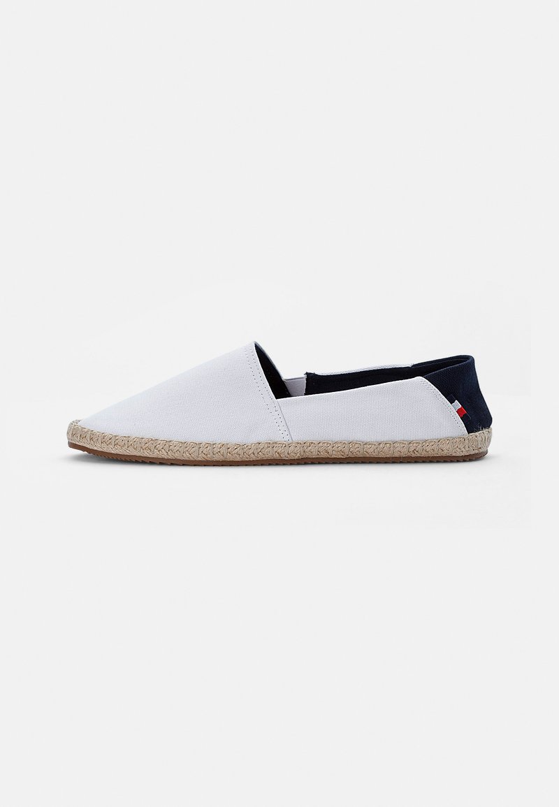 Hvit lerrets espadrille med spiss tå, elastiske sidestykker og såle av naturlig jute-seil. Har en marineblå aksent ved hælen.