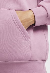 Svetlo vijolična majica z dolgimi rokavi z žepom kenguruja, rebrastimi manšetami in mehko teksturo tkanine. Vidni so podrobni šivi.