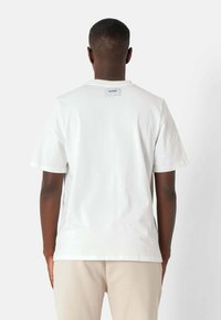 Hvid bomulds t-shirt med en afslappet pasform, korte ærmer og et firkantet syet skilt på den bagerste hals. Glat tekstur, ensfarvet.