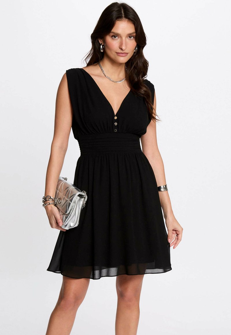 Robe noire avec un décolleté en V profond, manches courtes, taille froncée et jupe évasée. Présente trois boutons à l'avant. Pochette argentée.