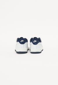 Baskets blanches avec des accents bleu marine, tige en cuir lisse, col rembourré et logo au talon. La semelle en caoutchouc offre stabilité et adhérence.
