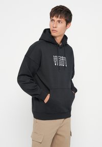 Μαύρη μ hoodie με καγκουρό τσέπη μπροστά, με εκτυπωμένο λευκό γραφικό σχέδιο "VISION." Φτιαγμένη από απαλό ύφασμα, με κουκούλα που ρυθμίζεται με κορδόνι.