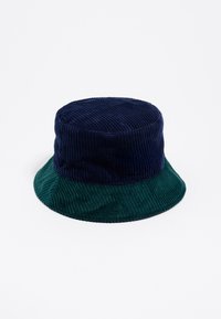 Kapelusz typu bucket wykonany z korduroyu, z granatową górą i ciemnozielonym rondem. Posiada pionową, prążkowaną teksturę oraz szeroki, miękki, opadający brzeg.