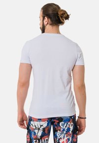 Weißes Kurzarm-T-Shirt, taillierte Passform, aus Baumwollmaterial. Getragen mit bunten Cargo-Hosen mit Mustern in Blau, Rot und weißen Spritzdesigns.