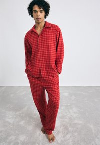 Red checkered loungewear set made of soft fabric; features long-sleeve button-up shirt and matching pants with a relaxed fit.