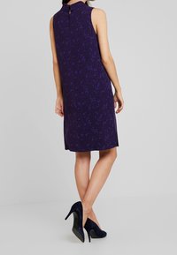 Bezramieniowa fioletowa sukienka z kwiatowym wzorem, z dekoltem w kształcie łezki na plecach i luźnym krojem. Połączona z granatowymi szpilkami.