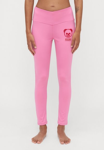 Leggings roses en tissu extensible, avec une taille haute et un logo d'ours brodé en rouge. Texture lisse, design ajusté.