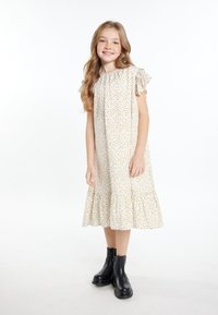 Hvid kjole med gul blomstret print, voluminøse korte ærmer og en tieret kant. Kombineret med sorte ankelstøvler. Casual design.