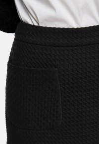 Black textured skirt with a raised pattern, features a side pocket and a wide waistband. Material appears soft and slightly stretchy.