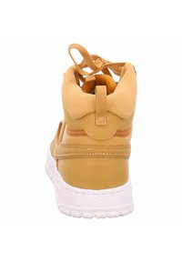 Baskets montantes en synthétique beige avec un col rembourré, semelle en caoutchouc blanche et accents texturés. Présente des lacets et une languette de tirage.