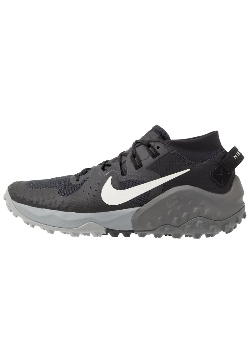 Scarpa sportiva nera e grigia con una tomaia testurizzata, il logo Nike bianco e un suola robusta. Presenta un profilo basso per garantire flessibilità.