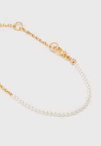 Λεπτό βραχιόλι με μικρές λευκές πέρλες και χρυσή αλυσίδα που καταλήγει σε χρυσό κούμπωμα με μικρό διαφανές διακοσμητικό λίθο.