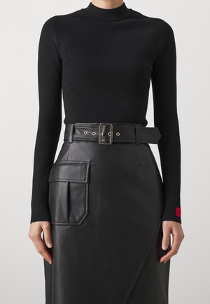 Vrouw draagt een zwarte coltrui met lange mouwen en een zwarte leren rok met hoge taille, riem en grote zijzak.