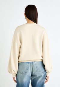 Beige oversized sweatshirt med ballongsleeves, myk tekstur og rund hals, paired med lyseblå high-waisted jeans.