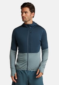 Huvtröja med dragkedja i mörkblått och ljusblått, med strukturerad tyg, tumhål och sömlös färgblockeringsdesign.