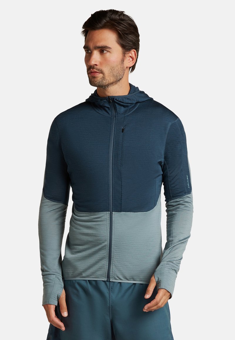 Huvtröja med dragkedja i mörkblått och ljusblått, med strukturerad tyg, tumhål och sömlös färgblockeringsdesign.