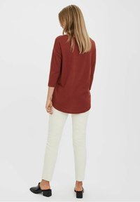 Haut à manches longues bordeaux à coupe décontractée, porté avec un pantalon droit de couleur crème et des chaussures noires à talons blocs. Texture lisse, design simple.