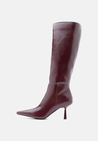 Bota de cuero burdeos hasta la rodilla con punta afilada, acabado brillante y tacón de aguja delgado. Textura suave con una silueta elegante.