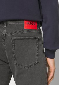 Svarta jeans med en framträdande röd "HUGO"-etikett, med rak passform, standardfickor och en mjuk denimstruktur.