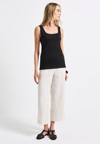 Top senza maniche di colore nero con scollatura quadrata, abbinato a pantaloni larghi in lino color avorio e sandali intrecciati neri.