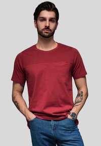 Rød bomulds tshirt med en struktureret panel over brystet, korte ærmer og rund halsudskæring. Bæres sammen med blå denim jeans og minimal hardware.