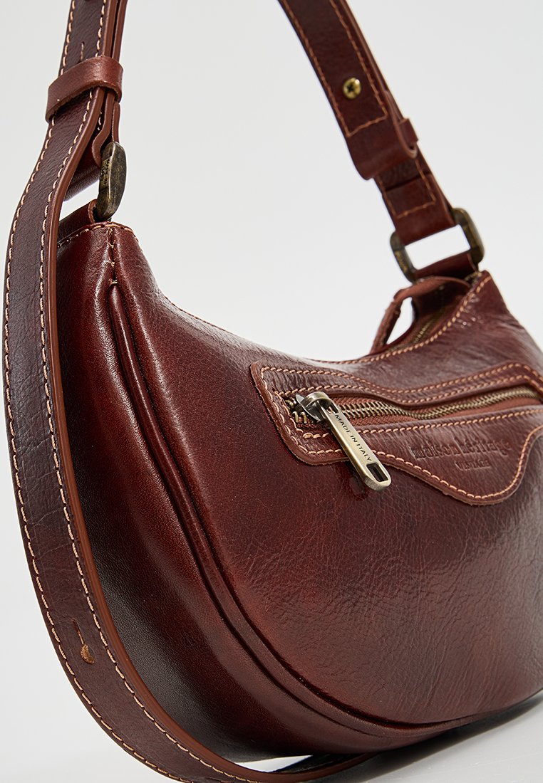 Brązowa skórzana torebka o gładkiej teksturze, zakrzywionym kształcie, kieszeni na zamek błyskawiczny i regulowanym pasku na ramię. Kontrastowe detale przeszycia.