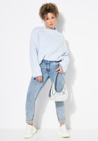 Suéter de canalé azul claro, vaqueros azules con los puños enrollados, zapatillas blancas y un bolso metálico plateado. La textura parece suave y acogedora.