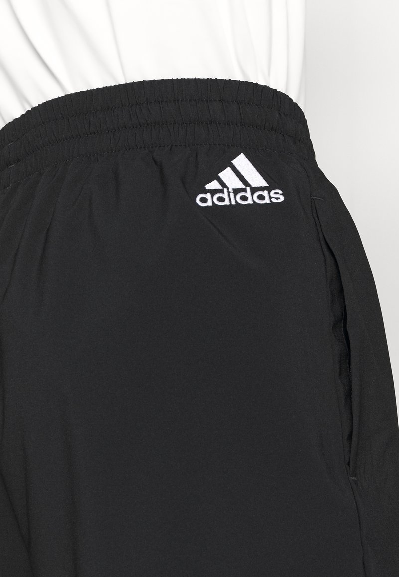 Mustat urheiluhousut, jotka on valmistettu kevyestä kankaasta. Housuissa on joustava vyötärönauha ja vasemmassa lantiossa valkoinen Adidas-logo.
