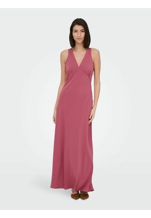 Femme debout portant une robe sans manches rose poudré longue jusqu'au sol, avec un col en V et des ballerines pointues marron sur un fond clair uni.