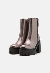 Botas de tobillo metálico gris con una plataforma y tacón negro grueso, que cuentan con una cremallera lateral y una textura suave. Diseño de punta redonda.