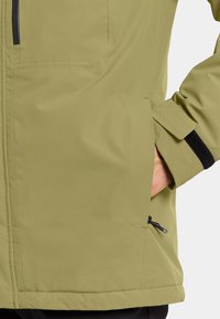 Veste verte en tissu texturé, dotée d'une poche zippée, de poignets ajustables et d'un cordon élastique au bas.
