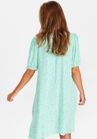 Miętowa sukienka z krótkimi bufkami, luźny krój i rozproszony niebieski wzór. Lekka tkanina o miękkiej teksturze.