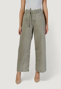 Jeans de pierna ancha en gris claro con cinturilla anudada, que cuentan con bolsillos delanteros y una textura ligeramente desgastada, combinados con tacones en tonos neutros.