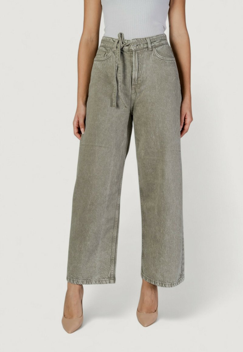 Jeans de pierna ancha en gris claro con cinturilla anudada, que cuentan con bolsillos delanteros y una textura ligeramente desgastada, combinados con tacones en tonos neutros.