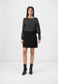 Haut noir à manches longues avec un motif de petits pois blancs, associé à une mini-jupe noire. Le modèle porte des bottines noires et tient un petit sac noir.