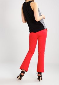 Top sin mangas de estampado en blanco y negro con la espalda descubierta, combinado con pantalones acampanados rojos. El modelo lleva zapatos de tacón alto negros con cordones.