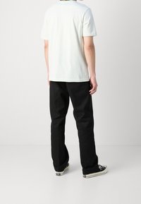 Světle zelené bavlněné tričko s volným střihem, krátkými rukávy a kulatým výstřihem, spárované s černými kalhotami a černými teniskami.