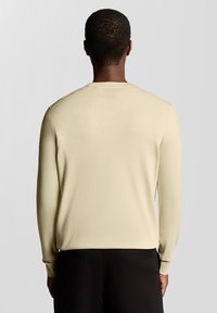 Camisola de manga comprida amarelo claro com gola redonda e punhos canelados, feita de tecido macio e texturizado. Sem padrões ou ferragens visíveis.