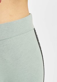 Lysegrønne joggebukser med elastisk midjebånd, sidelommer og en glatt, teksturert stoff med en ensfarget overflate.