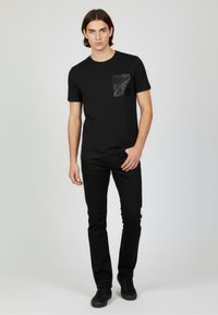 Black cotton T-shirt with a textured black pocket, paired with black slim-fit jeans and black sneakers, featuring a smooth finish.