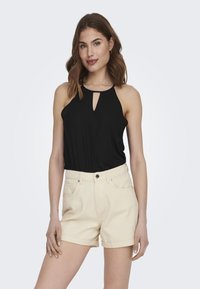 Top sin mangas negro con un detalle de ojal y pantalones cortos de talle alto en color beige claro. La tela parece suave; los pantalones cortos tienen dobladillos enrollados y bolsillos.
