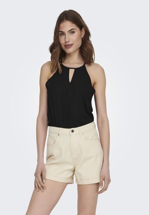 Top nero senza maniche con dettaglio a oblò e pantaloni corti a vita alta color beige chiaro. Il tessuto appare liscio; i pantaloni corti presentano risvolti e tasche.