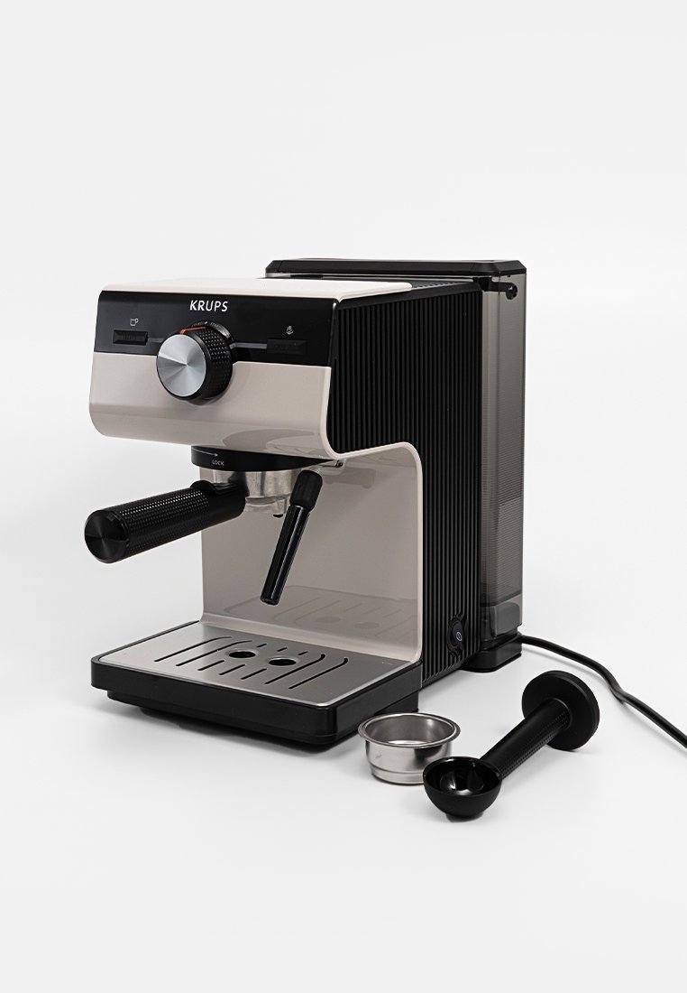 Kaffeepadmaschine mit elegantem Design, ausgestattet mit einem Dampfstab, einem Siebträger und einem Metallstampfer auf einer Arbeitsplatte.