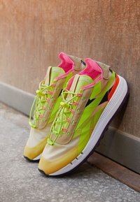 Chaussures de sport lumineuses vertes et jaunes avec des accents roses, en matériau mesh léger et une semelle texturée. Système de laçage unique améliorant le maintien.