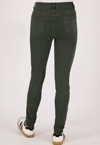 Groene high-waisted skinny jeans met achterzakken, een gladde textuur en een slim fit, gecombineerd met witte sneakers met zwarte accenten.