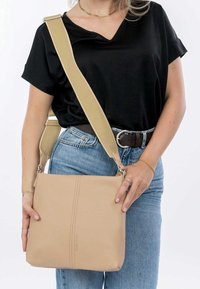 Beżowa skórzana torba crossbody o teksturowej powierzchni i szerokim, regulowanym kremowym pasku. Posiada centralny detal szwu oraz srebrne akcesoria.