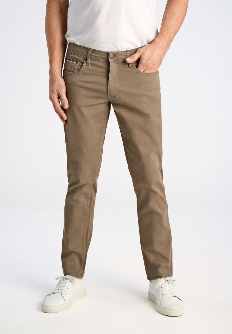 Pantalones de algodón caqui con un diseño de pierna recta, cinco bolsillos y cierre de botón. Combinados con zapatillas deportivas blancas sobre un fondo neutro.