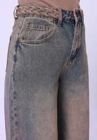 High-waisted, light blue denim wide-leg jeans with a braided belt. Features two front pockets and a faded texture. Seam detailing visible.